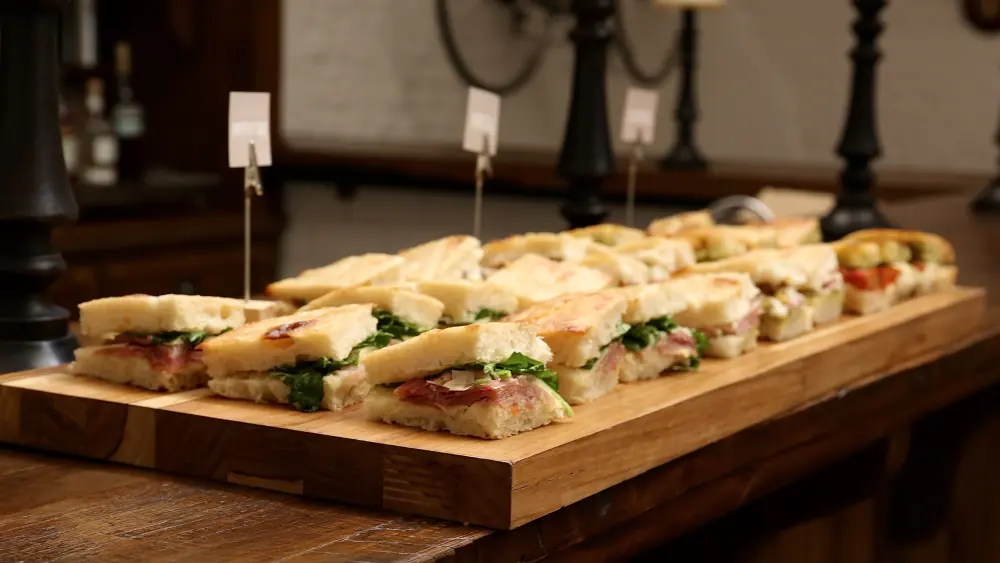 Paninis em porções individuais com plaquinhas sobre tábua de madeira