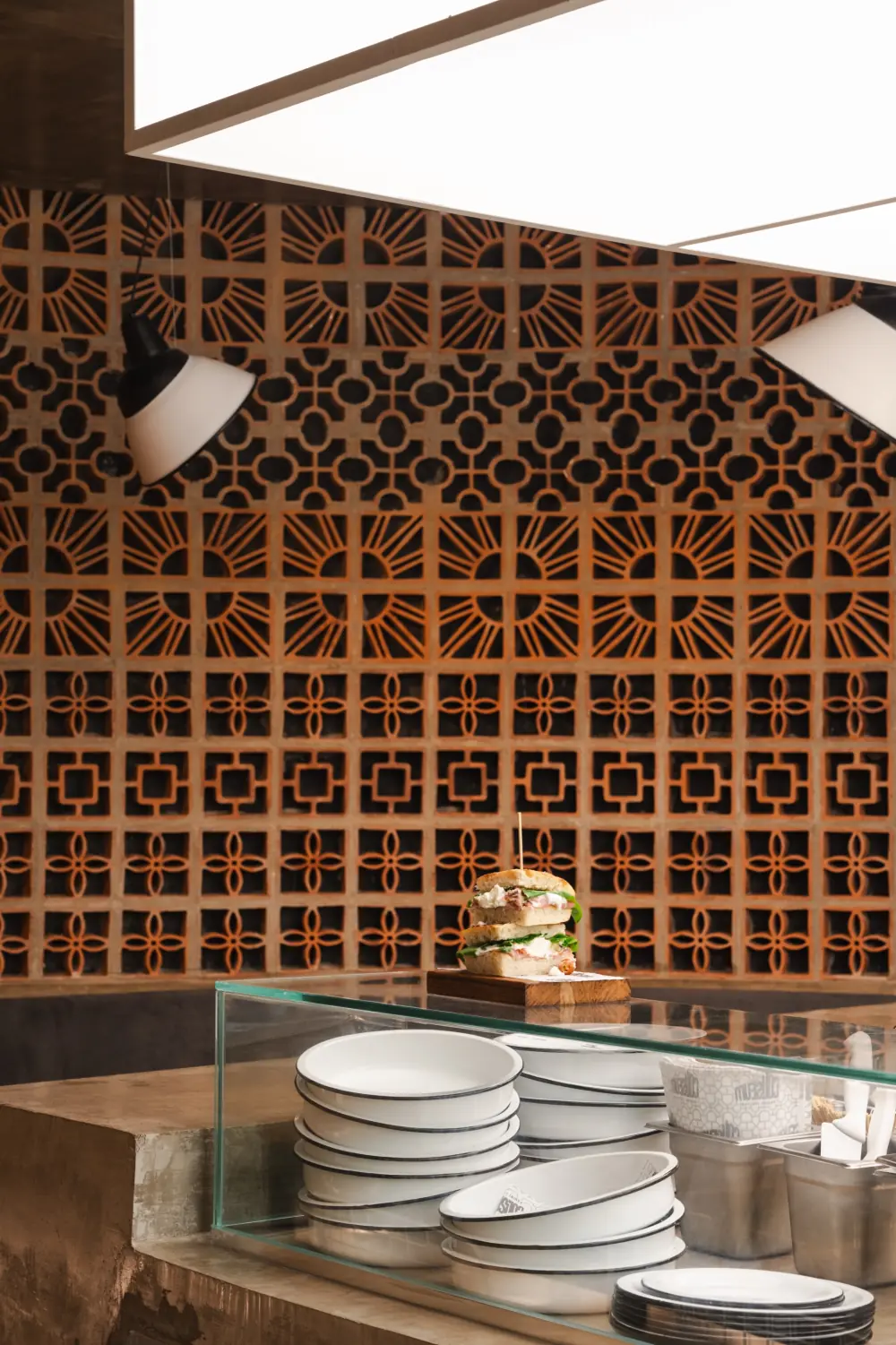 Parede de cobogó de terracota atrás da bancada, com panini e pratos de ágata