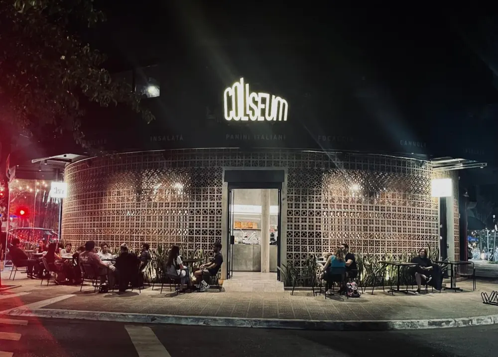 Fachada do Coliseum à noite, com mesas na calçada